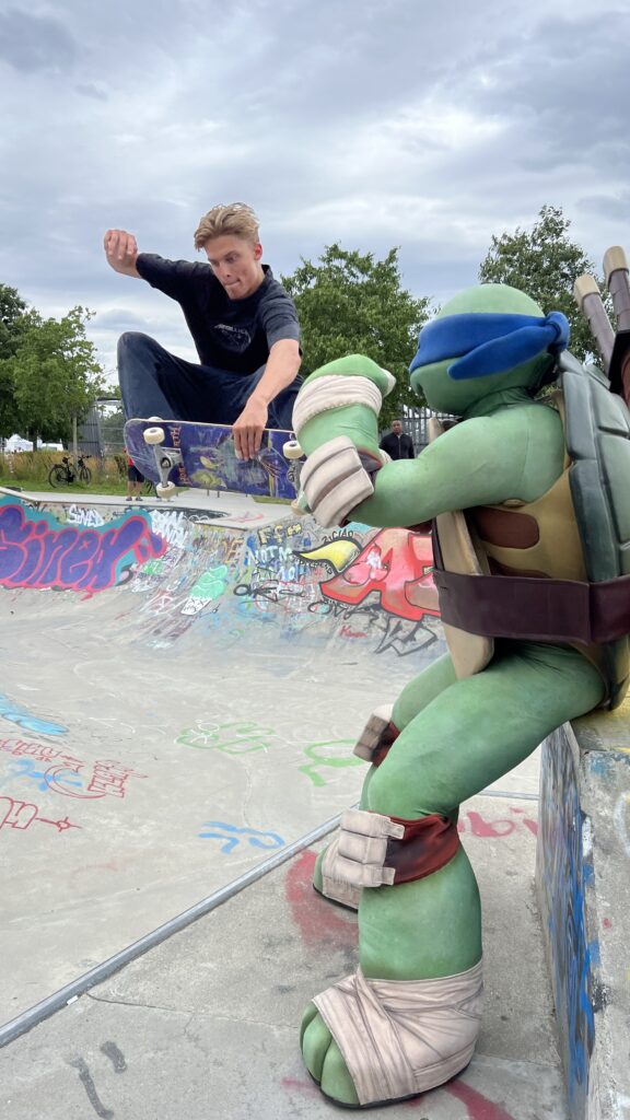Ein Skateboarder springt aus einer Bowl an einem Teenage Mutant Ninja Turtel vorbei.
