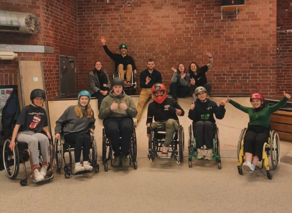 Eine Gruppe Jugendlicher in Rollstühlen  in einer Skatehalle. 