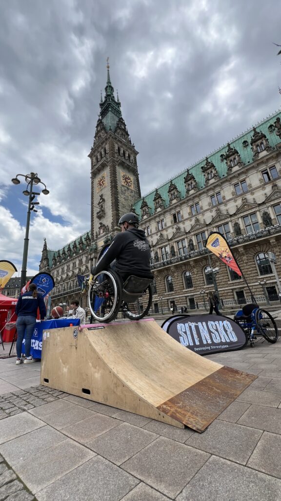 Ein Rollstuhlfahrer macht einen Trick auf den Hinterrädern balancierend an einer Quarter Ramp, die vor dem Hamburger Rathaus aufgestellt wurde.