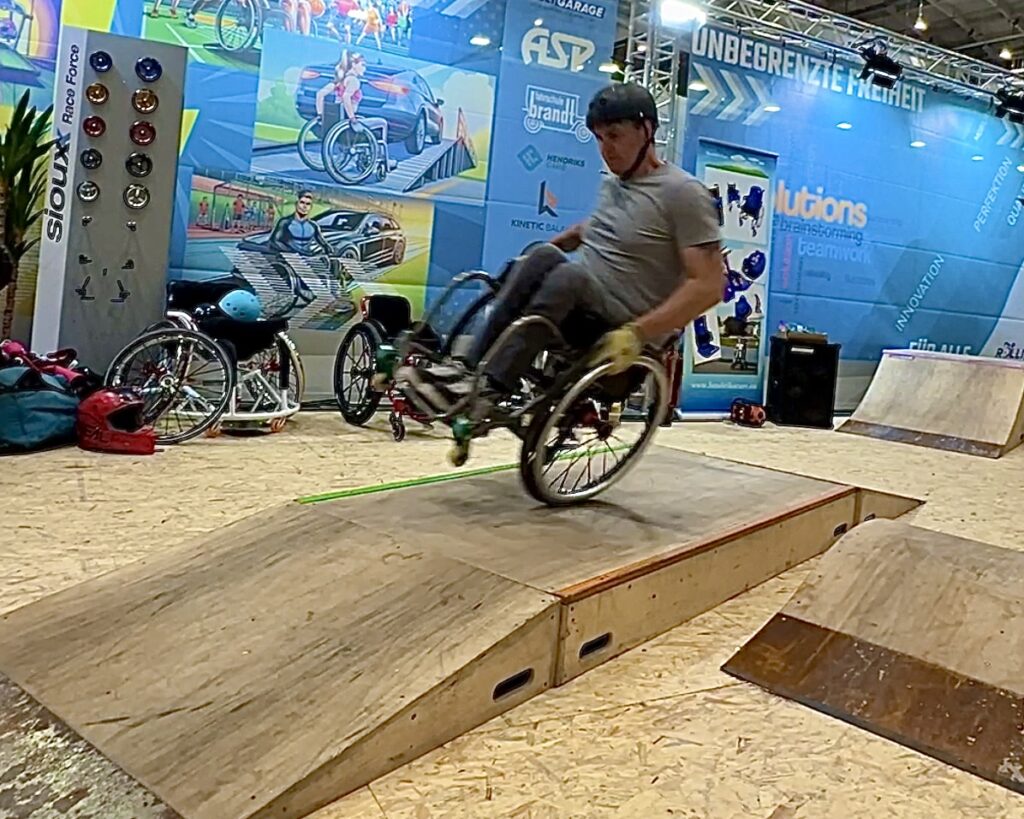 Rollstuhlfahrer fährt auf einem Rad über einen Skatepark auf einem Messestand. 