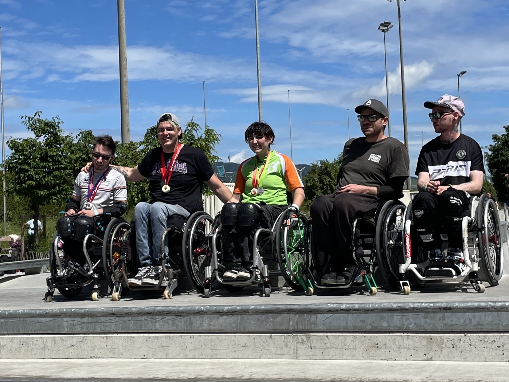 Im Skatepark stehen für die Siegerehrung fünf Rollstuhlfahrer nebeneinander, die ersten drei haben Medaillen. 