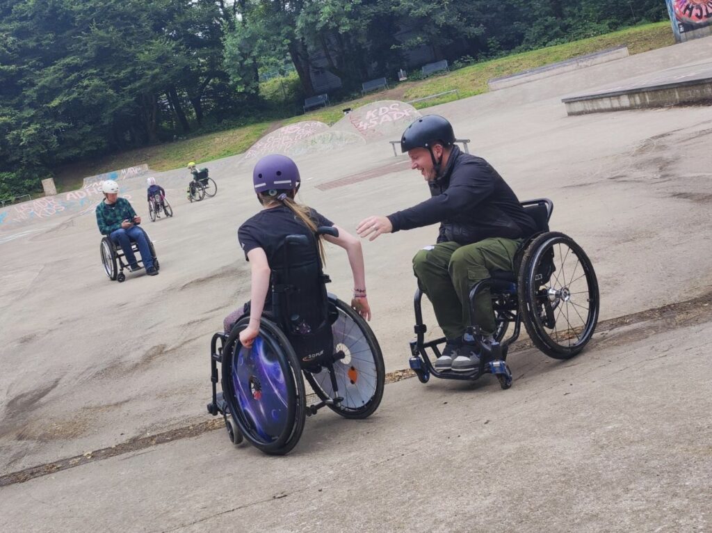 Rollstuhlfahrer im Skatepark. Ein Rollstuhlfahrer hilft einer Rollstuhlfahrerin eine Kante zu überwinden.