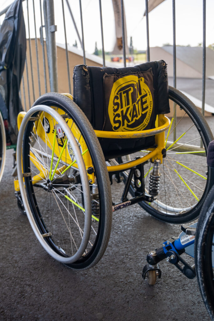 ein gelber Rollstuhl auf dem das Logo von SIT N SKATE auf der Rückenlehne ist