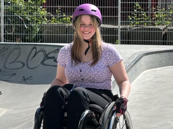 Eine Frau im Rollstuhl mit lila Helm im Skatepark