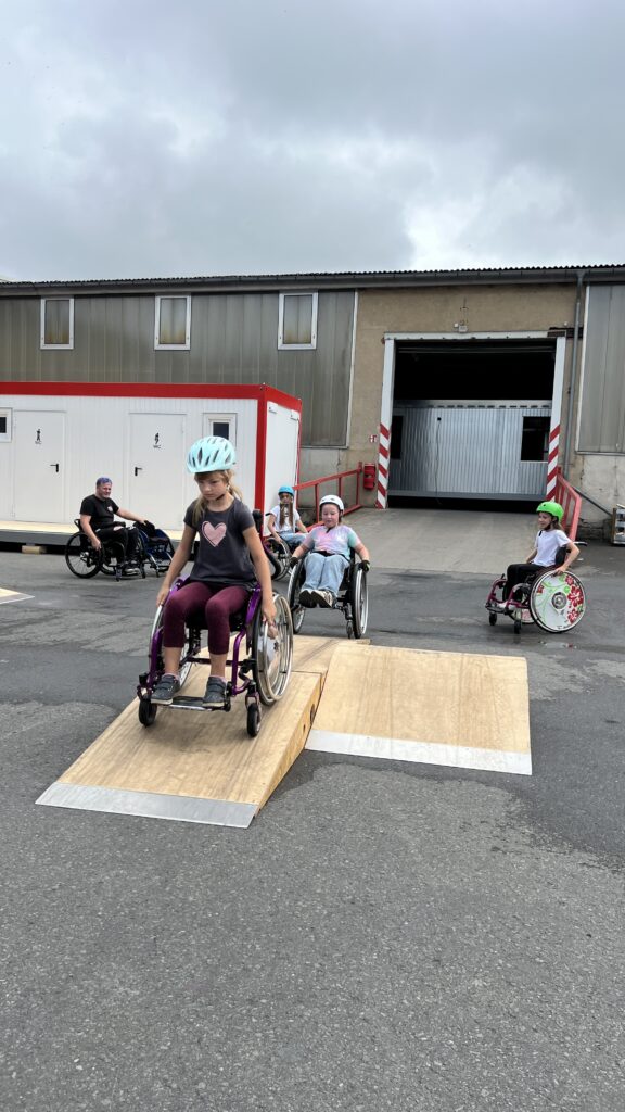 Kinder im Rollstuhl fahren über mobile Skate Rampen. 